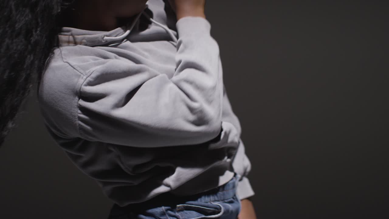 retrato de estudio de una mujer joven con capucha bailando con poca iluminación contra un fondo negro 3