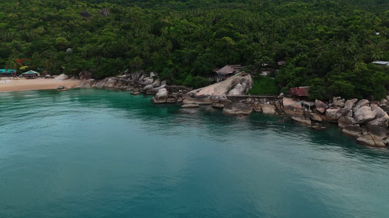 Aerial footage of a rocky beach with lush jungle and turquoise sea in Thailand. Scenic coastline, green forest, and tropical seascape. Perfect for travel, tourism, nature, and adventure projects.