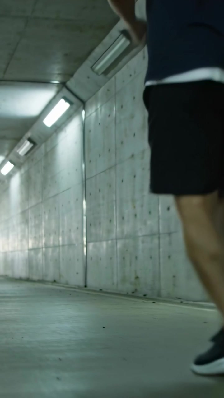 Video verticale: Corridore che entra da destra in un tunnel illuminato, in pantaloncini e scarpe da ginnastica, con spazio per il testo.