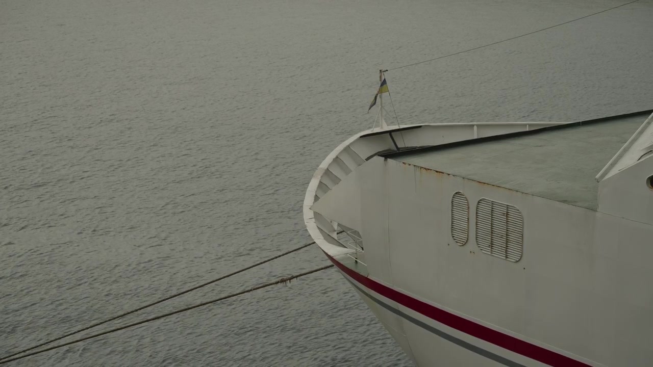 White ferry bow with red stripe cuts through flat grey sea under overcast sky with mooring ropes visible