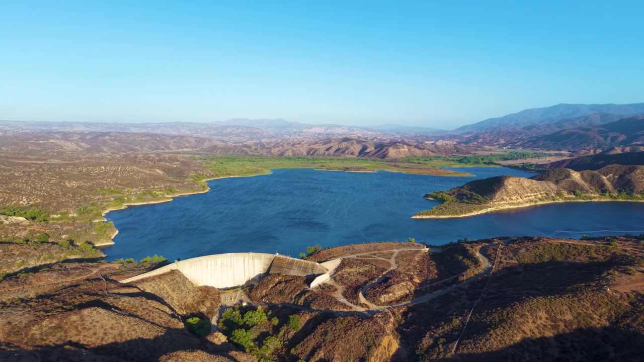 Vista aérea panorâmica de um belo e sereno lago nas montanhas da Califórnia. Céus azuis, águas azuis e margens verdes são vistos nesta espetacular tomada aérea acima da barragem do Lago Vail
