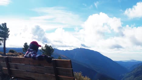 man sitting on a bench looking out into the mountain valley during a timelapse