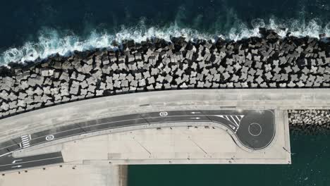 ocean waves crash on large breakwater jetty protecting marine port and road, drone top down