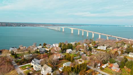 a distant drone shot of a long bridge standing over open water in rhode island with houses near by and taken during the day time