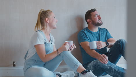 pareja decorando la habitación en casa sentada en el suelo tomando un descanso con una bebida caliente