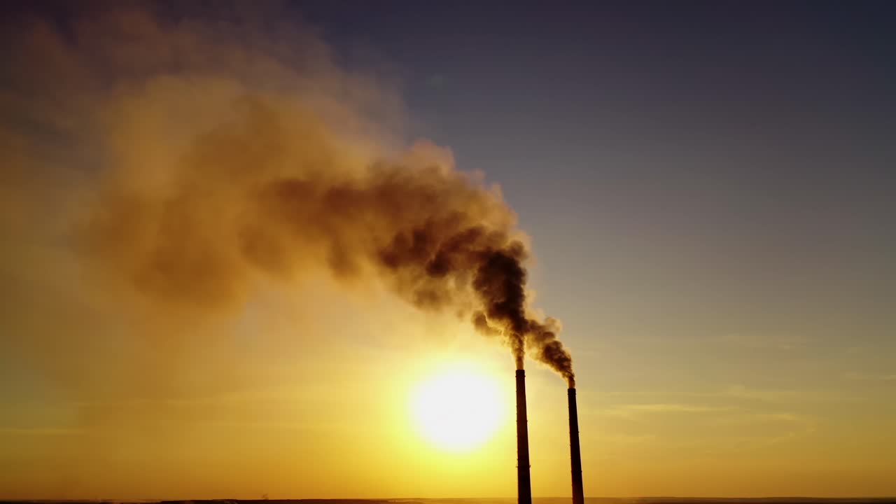 Dark smoke in the air. Two pipes from plant with chemical emissions in the sky at sunset. Ecological problems. Atmosphere in danger.