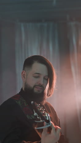 a bearded guitarist playing guitar in a blurry studio room with soft lighting, capturing the musician's focused expression and the blurred microphone in the foreground