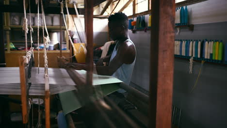 a young man operating a floor treadle loom inside