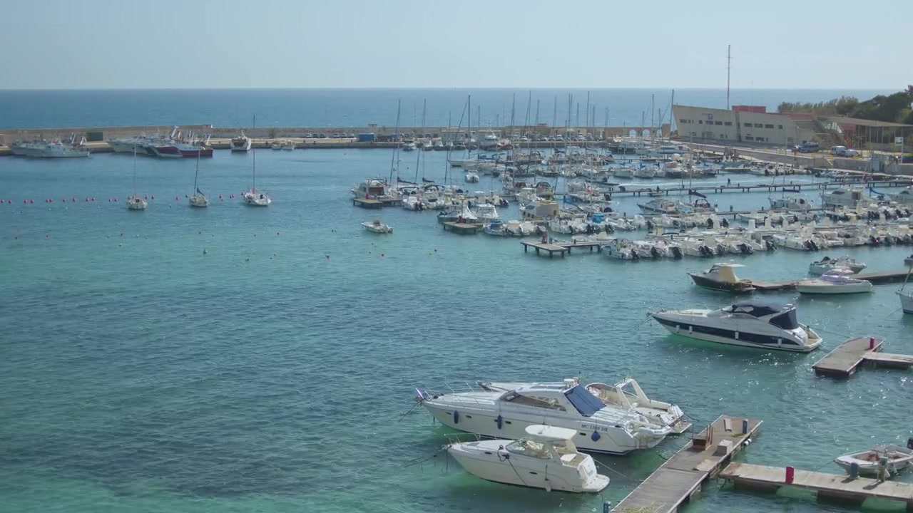 Yacht di lusso, barche a vela e motoscafi riempiono il porto turistico sulla costa adriatica della Puglia, Italia, mentre una moto d'acqua sfreccia nel porto durante una sequenza timelapse, vista statica elevata.