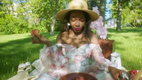 Black-Woman-eating-apple-and-adjusting-hair-on-picnic-in-park