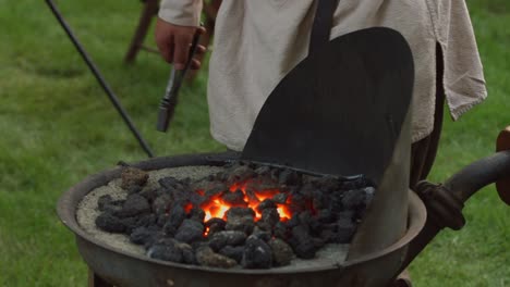 A-revolutionary-war-reinacter-blacksmith-puts-a-piece-of-metal-in-hot-coals-to-heat-up-while-he-pumps-the-bellows