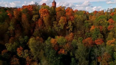 Toma-Aérea-Ascendente-De-árboles-Coloridos-Y-Castillo-De-Turaida-En-La-Cima-De-Una-Colina-Durante-El-Soleado-Día-De-Otoño-En-Letonia,-Europa