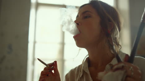 Creative-painter-blowing-smoke-out-in-studio.-Talented-girl-smoking-indoors.