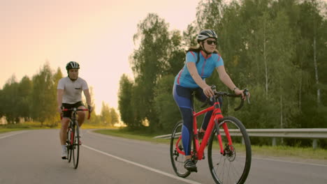 Front-view-of-a-young-couple-or-friends-riding-their-bikes-in-the-city-park-or-boulevard-in-summertime.-People-leisure-and-lifestyle-concept