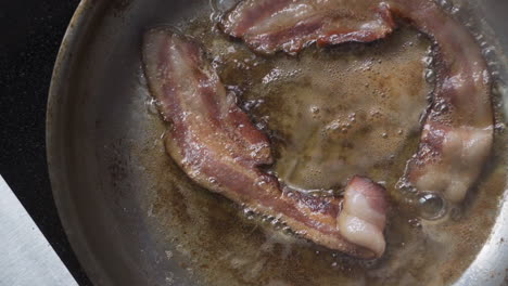 overhead crispy bacon frying in hot, greasy pan for morning breakfast