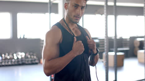 young biracial trainer with short dark hair and stubble holding jump rope in gym
