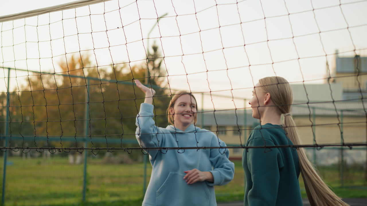 팀 동료들이 함께 점프하고, 배구공을 망으로 돌려보내며, 웃으며, 야외 배구 경기에서 승리하기 위해 손을 잡고 축하합니다.