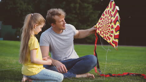 father and daughter sitting with a kite on meadow