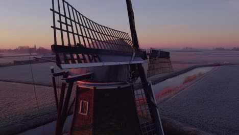 Orbit-shot-of-iconic-dutch-windmill-with-sun-shines-through-blades,-aerial