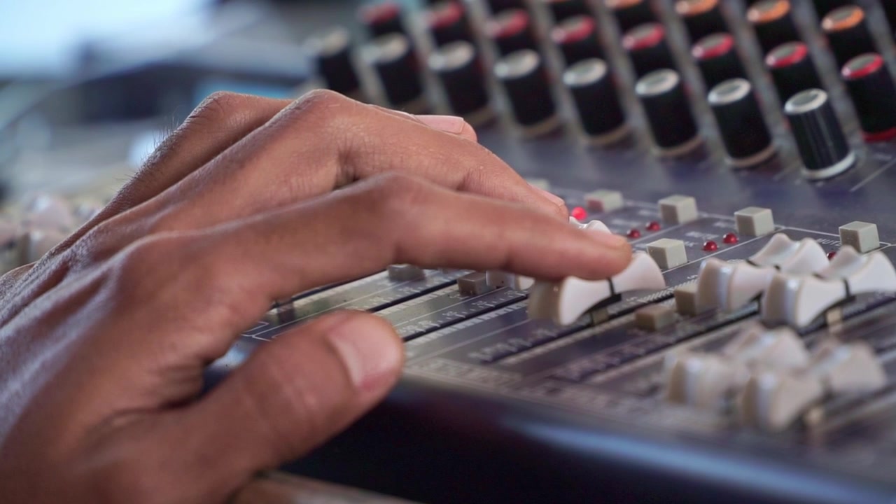 sound technician adjusting mixer knobs, audio console with LED meters, music production concept.