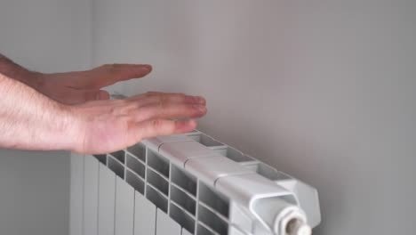 el hombre se calienta las manos con un radiador de calefacción