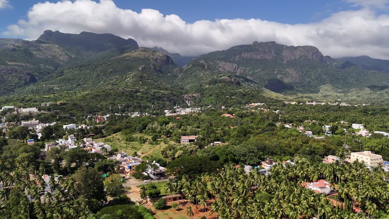 Majestic aerial panorama of the Western Ghats Courtallam, showcasing a forested valley town, flowing waterfalls, and monsoon clouds embracing the mountains