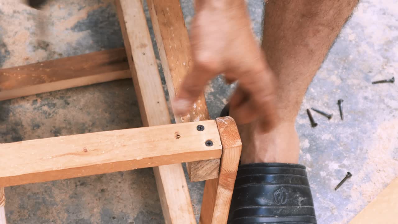 Abile falegname che usa un trapano elettrico per avvitare viti in una piccola sedia di legno nel suo laboratorio artigianale per vendere e sostenere l'economia locale