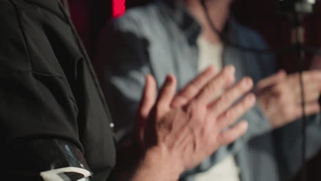 close-up of two people clapping hands expressively in a soundproof recording studio during a mid-performance. the scene focuses on the dynamic movement of hands in front of a microphone stand