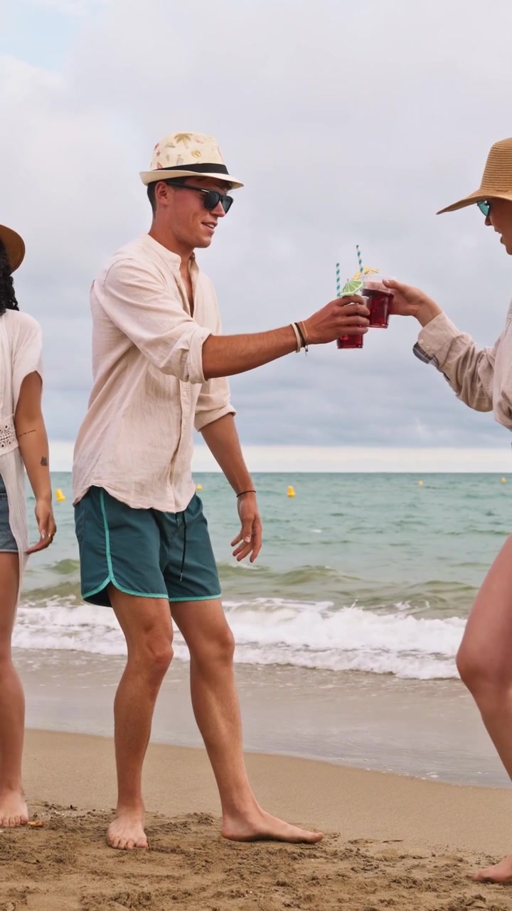 Gruppo di amici che ballano e bevono cocktail in spiaggia