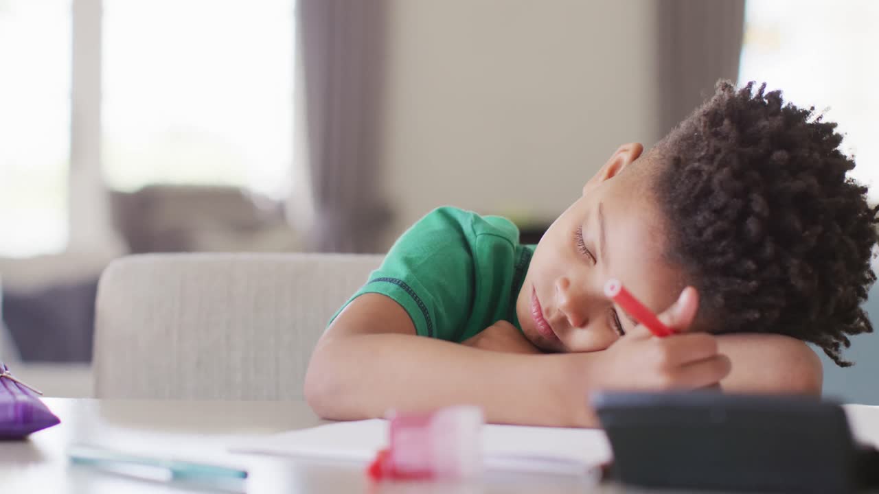 Ragazzo afroamericano felice seduto al tavolo, che fa i compiti e dorme.