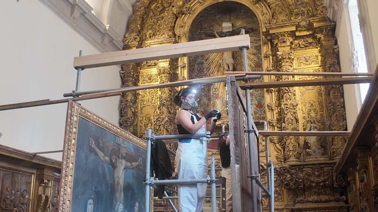 Restoration worker on scaffolding cleans intricate gold details in Porto Cathedral altar area