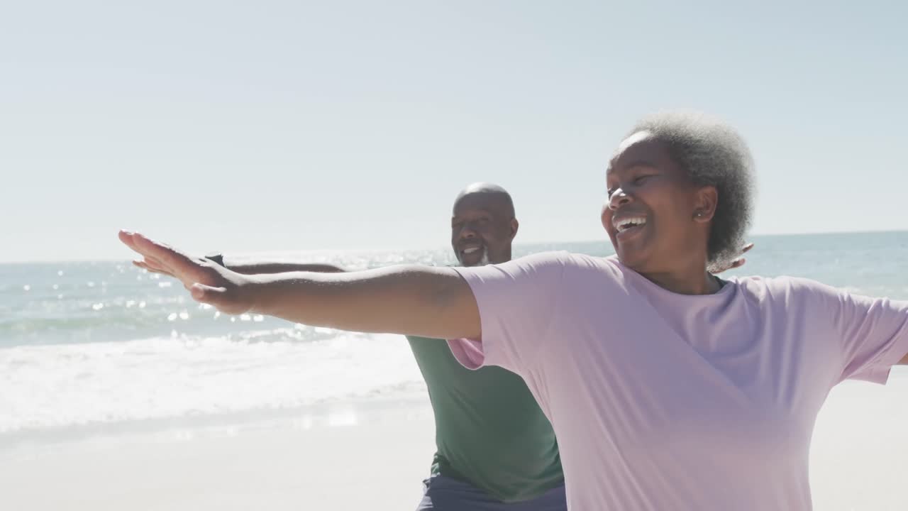 Felice coppia anziana afroamericana che fa yoga e stretching in spiaggia, al rallentatore.