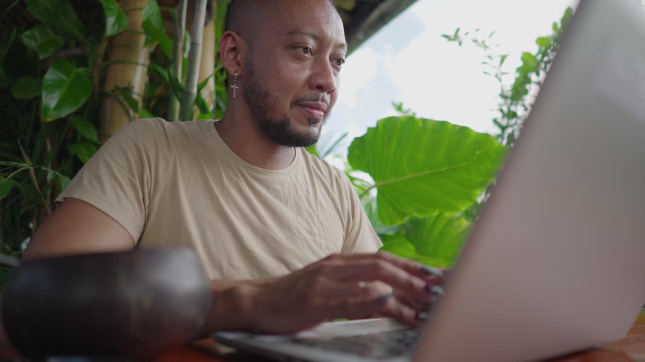 Man working on a laptop in a tropical cafe