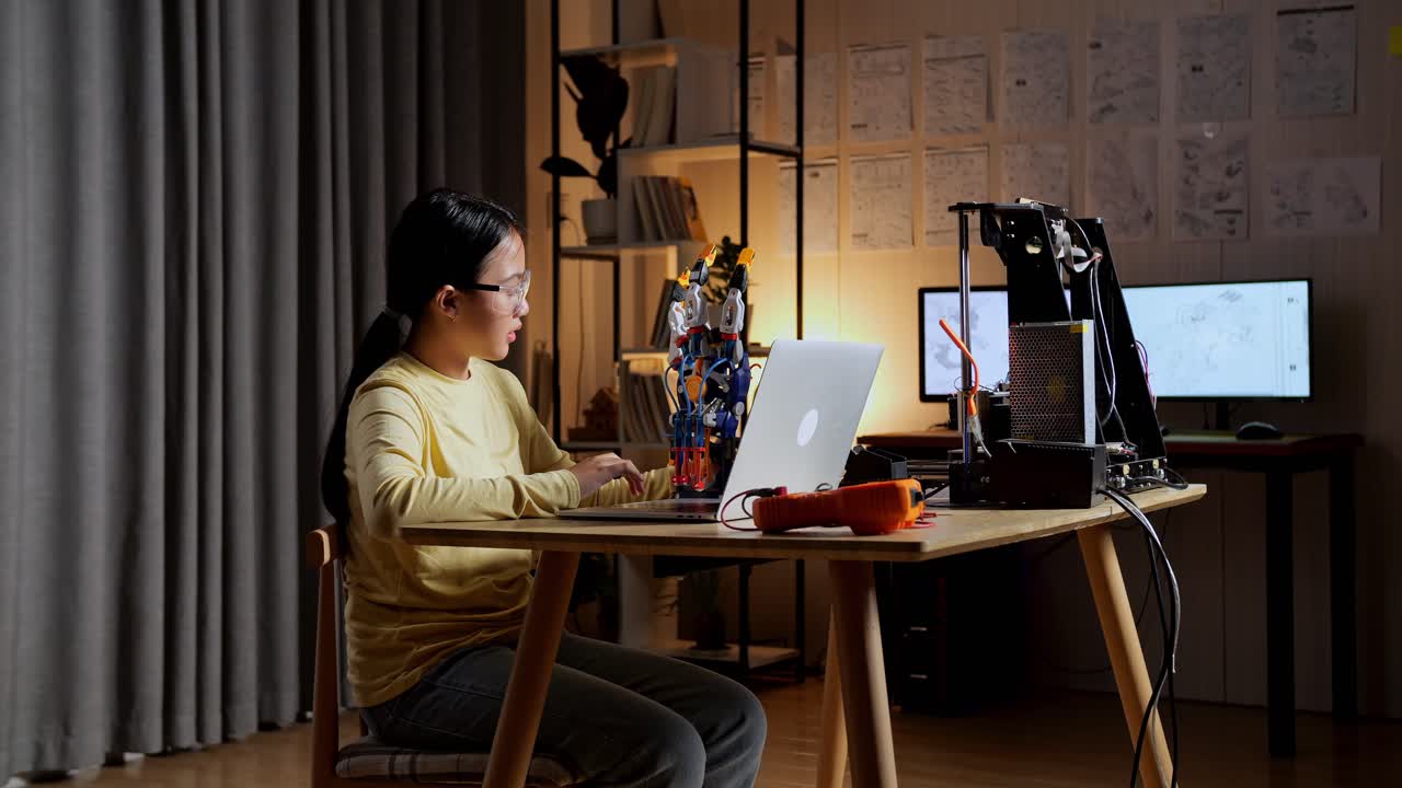 십대 아시아 소녀가 집에 있는 노트북의 사진과 사이보그 손을 확인하고 비교하고 있습니다.