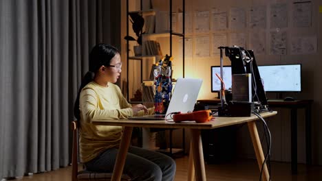 teen asian girl checking and comparing a cyborg hand to the picture on a laptop at home