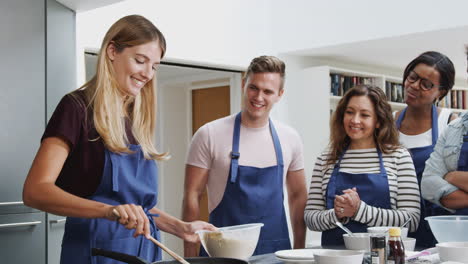 female teacher making flatbread on cooker in cookery class as adult students look on