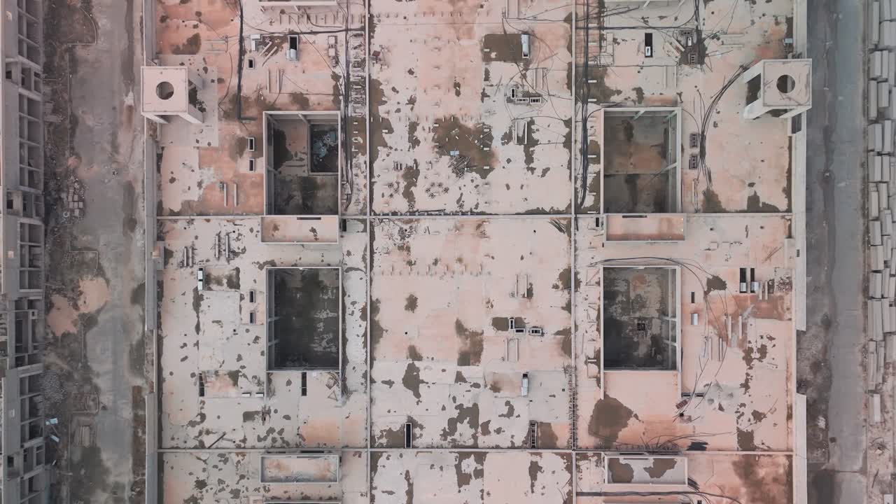 Overhead drone of a rectangular abandoned block in Kuwait roof void grid, stains, exposed cables and shafts, symmetrical plan between service roads clean demolition survey visual no people