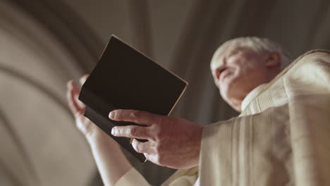 caucasian old clergyman reading holy bible in church