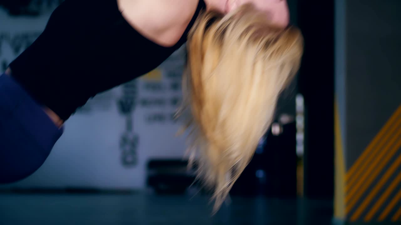close-up, attractive blonde woman in black top, upside down with flowing hair performs exercises on  loops, Straps in the gym