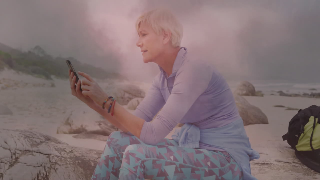 woman using smartphone on rocky beach, displaying floating analytics charts for tech presentation