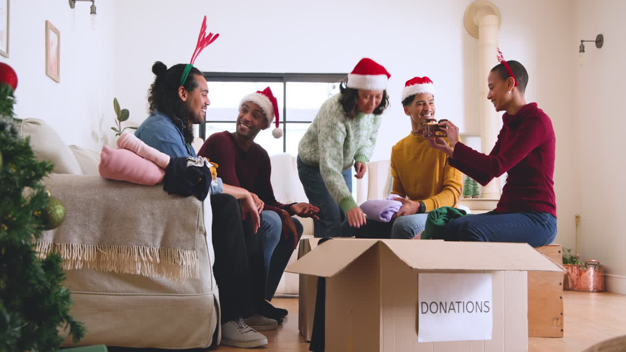 At christmas, young diverse friends wearing festive hats packing clothes for donations at home