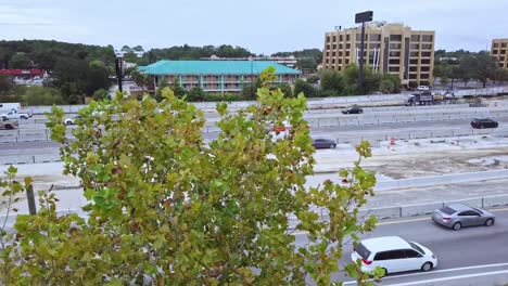 low aerial panning drone shot of busy highway with road construction zone showing cars and trucks with treetop in foreground and buildings in background