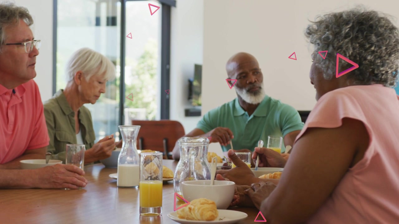 Diverse seniors sitting at table by door, woman in pink top talking, animated triangles floating