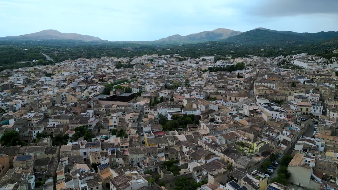 A stunning aerial shot of Artà, a historic town in Mallorca, showcasing the dense Spanish terracotta-tiled architecture and the surrounding natural landscape of rolling hills and mountains