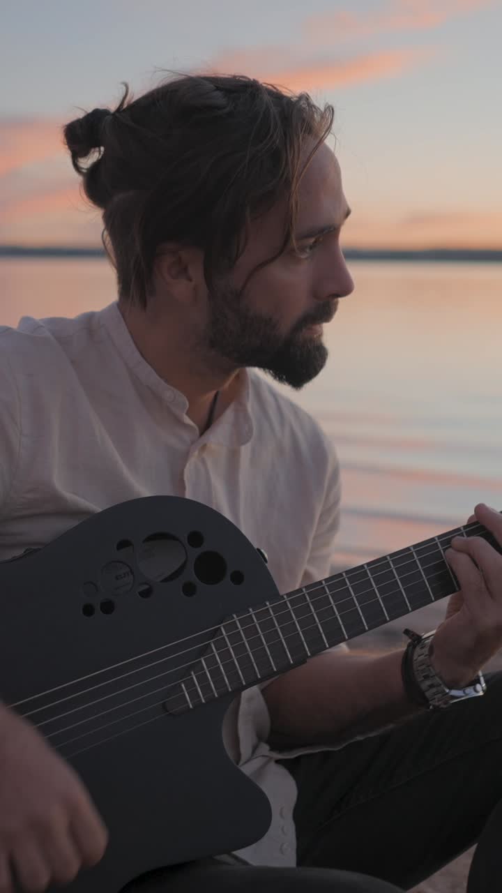 Man playing acoustic guitar at sunset by the water