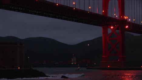 small boats passing under the golden gate bridge at night are dwarfed by the enormous structure