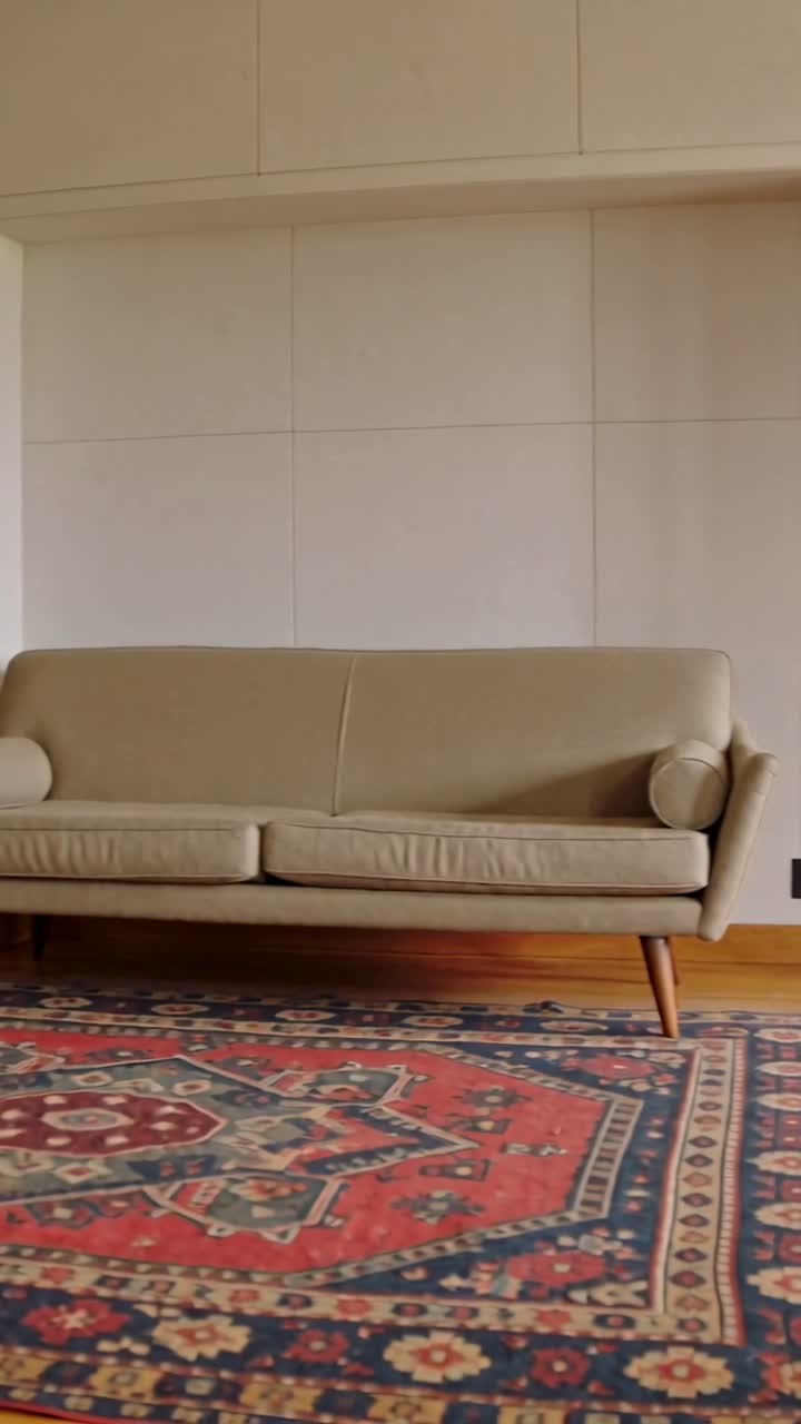 Vertikal video: Kamera panorerer fra et træskab, bevæger sig til venstre i et hjem mod en centreret beige to-personers sofa.