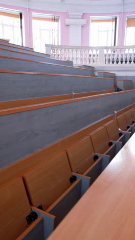 rows of long desks in conference hall. empty auditorium in the modern educational center. wooden tables without students in large comfortable classroom. vertical video