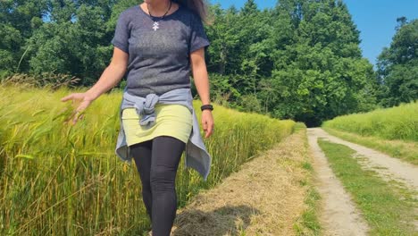 a woman strolls beside a golden wheat field on a breezy, sunny spring day in switzerland, gently brushing her hand through the swaying grain as her hair flows in the wind