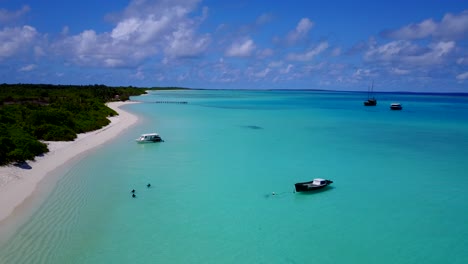 aerial view of turqoise beach of a caribbean island while small boats are floating in shallow waters by the sea